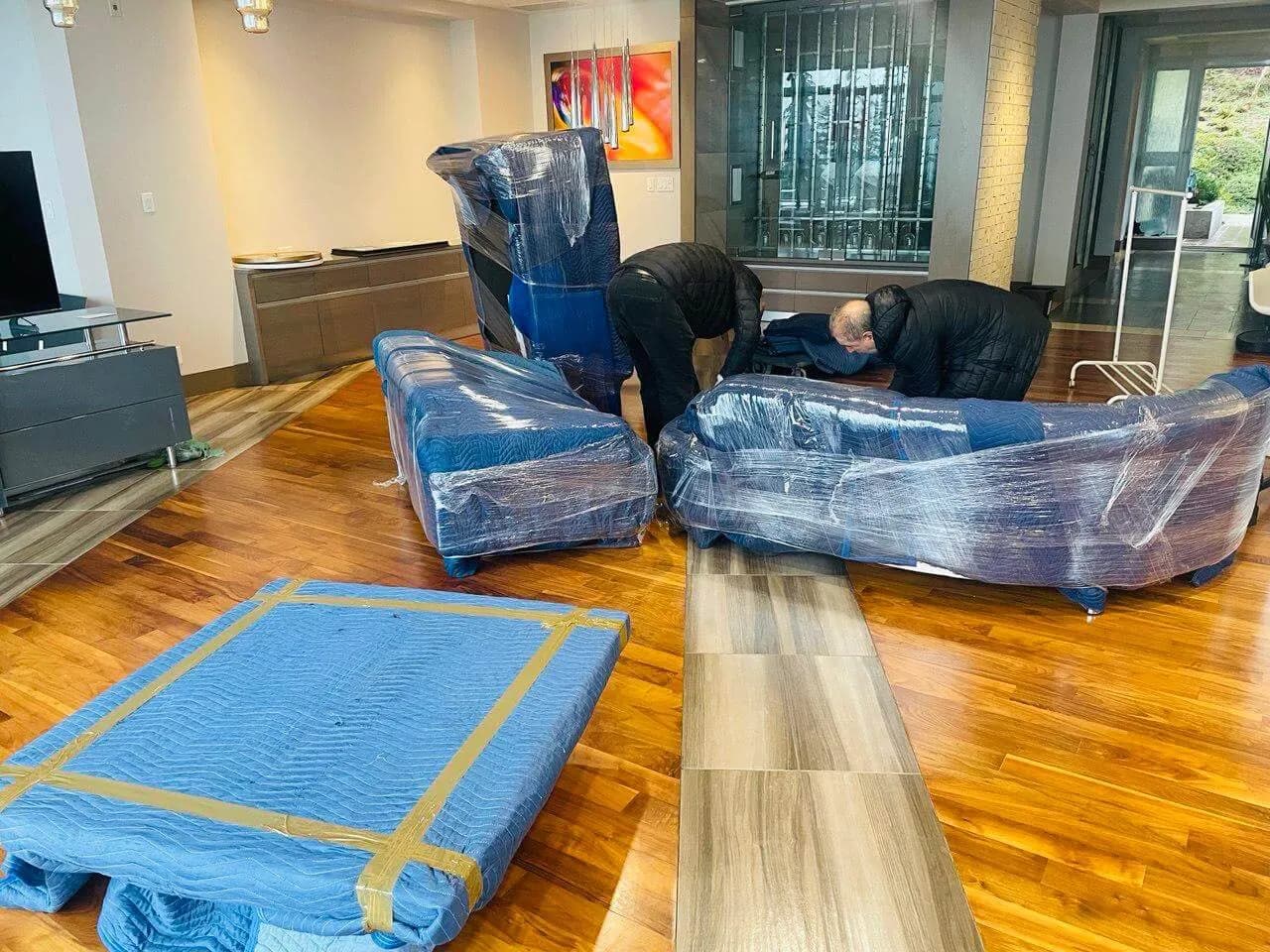 Moving team carefully protecting furniture with moving blankets and stretch wrap